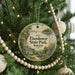 A round ornament hanging on a Christmas tree, featuring a scenic landscape with a house, trees, and a body of water.