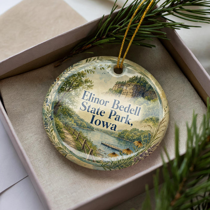 A decorative ornament in a box, featuring a scenic landscape with a river, mountains, and greenery.