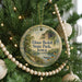 A round ornament hanging on a Christmas tree, featuring a scenic landscape with a river and a bridge.