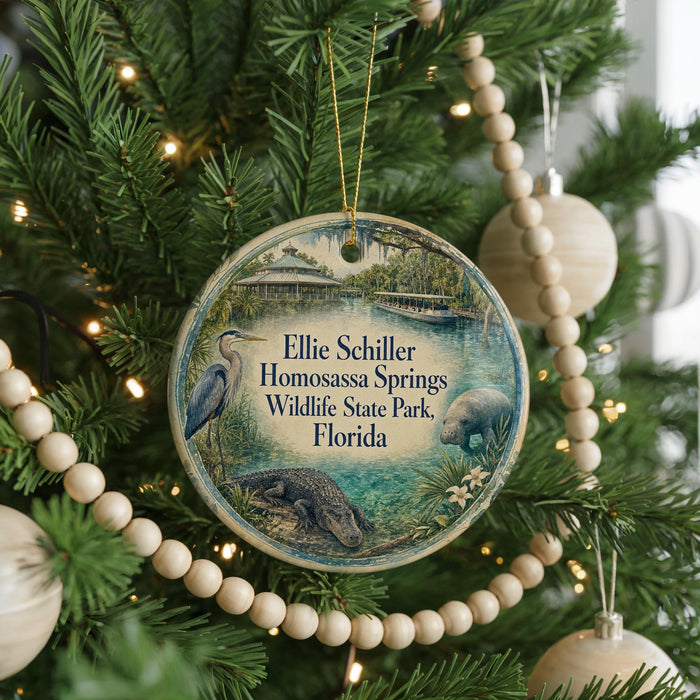 A round ornament hanging on a Christmas tree, featuring an illustration of a bird, a beaver, and a crocodile, with text that reads "Ellie Schiller Homosassa Springs Wildlife State Park, Florida".