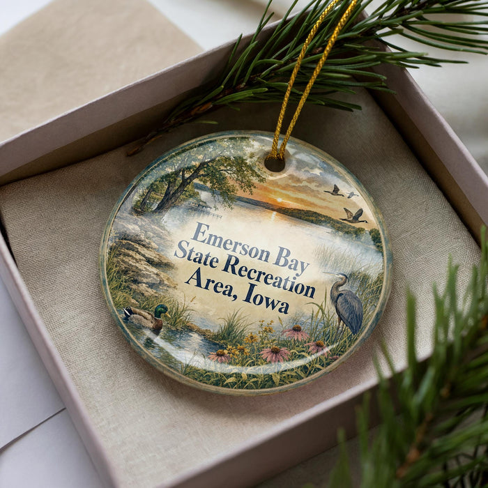 A decorative ornament in a box, featuring a scenic landscape with a lake, trees, and birds.