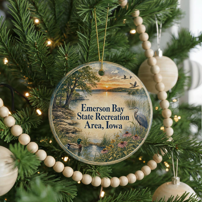 A round ornament hanging on a Christmas tree, featuring a scenic landscape with a lake, trees, and birds.