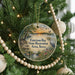 A round ornament hanging on a Christmas tree, featuring a scenic landscape with a lake, trees, and birds.
