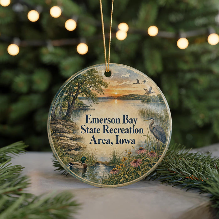 A round ornament with a scenic landscape featuring a lake, trees, and birds, hanging from a string.