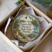 A round ornament with a bird and a seal, placed in a box with a white tissue paper lining.