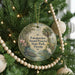 A round ornament hanging on a Christmas tree, featuring a scenic illustration of a tropical landscape with palm trees, a bird, and a body of water.