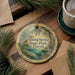 A decorative ornament with the text "Fanning Springs State Park, Florida" on it, surrounded by pine branches and a cup of coffee on a wooden surface.