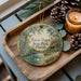 A wooden tray with a decorative ornament featuring a scenic landscape of Faverdys State Park, Florida, and pine cones.