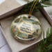 A decorative ornament in a box, featuring a scenic image of Fayette Historic State Park, Michigan.