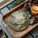 A decorative ornament featuring a scenic landscape of Fernne Clyffe State Park, Illinois, with pine cones and a lit candle on a wooden tray.