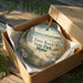 A decorative ornament in a wooden box, featuring a scenic image of a beach and park.