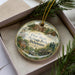 A decorative ornament in a box, featuring illustrations of historic buildings and people, with the text "First State Heritage Park, Delaware" prominently displayed.