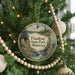 A round ornament hanging on a Christmas tree, featuring a scenic landscape with a lake, mountains, and a cabin.