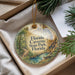 A round ornament with a scenic image of a forest and a winding path, surrounded by greenery, placed in a box with pine branches.