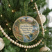 A circular ornament hanging on a Christmas tree, featuring a scenic landscape with mountains, a lake, and wildlife.