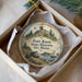 A round ornament with a picture of Fort Knox, Maine, and a cannon, placed in a box with a white tissue paper lining.