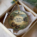 A round ornament with a picture of Fort Ross State Historic Park, California, and a barrel, hanging from a string.