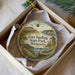 A round ornament with a painting of Fort Snelling, Minnesota, and a canoe, placed in a box with a white tissue paper lining.