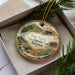 A decorative ornament in a box, featuring an illustration of Fort Verde State Historic Park, Arizona.