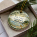 A decorative ornament in a box, featuring a scenic image of a fox in a field with a body of water in the background.