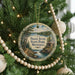 A round ornament hanging on a Christmas tree, featuring a scenic landscape with a lake and forest.