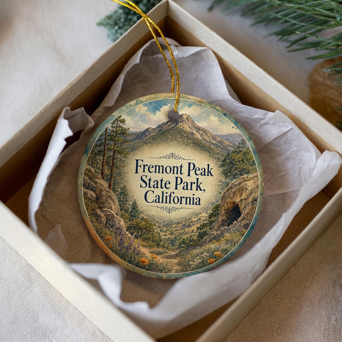 A decorative ornament in a box, featuring a scenic landscape with mountains, trees, and a winding path.