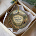 A decorative ornament in a box, featuring a scenic landscape with mountains, trees, and a winding path.