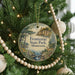 A round ornament hanging on a Christmas tree, featuring a scenic landscape with a lake and mountains.