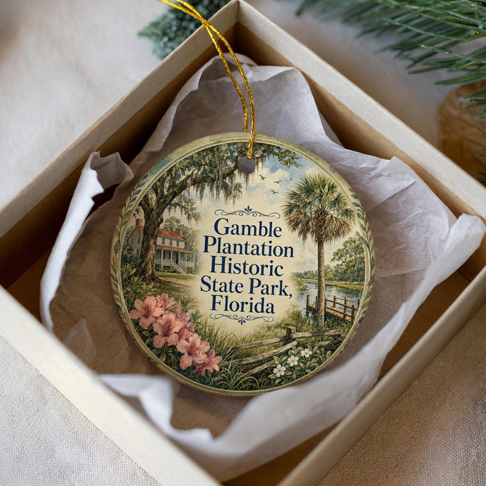 A round ornament with a painting of a house and palm trees, hanging from a string inside a box.