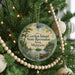 A round ornament hanging on a Christmas tree, featuring a scenic landscape with a lake and a canoe.