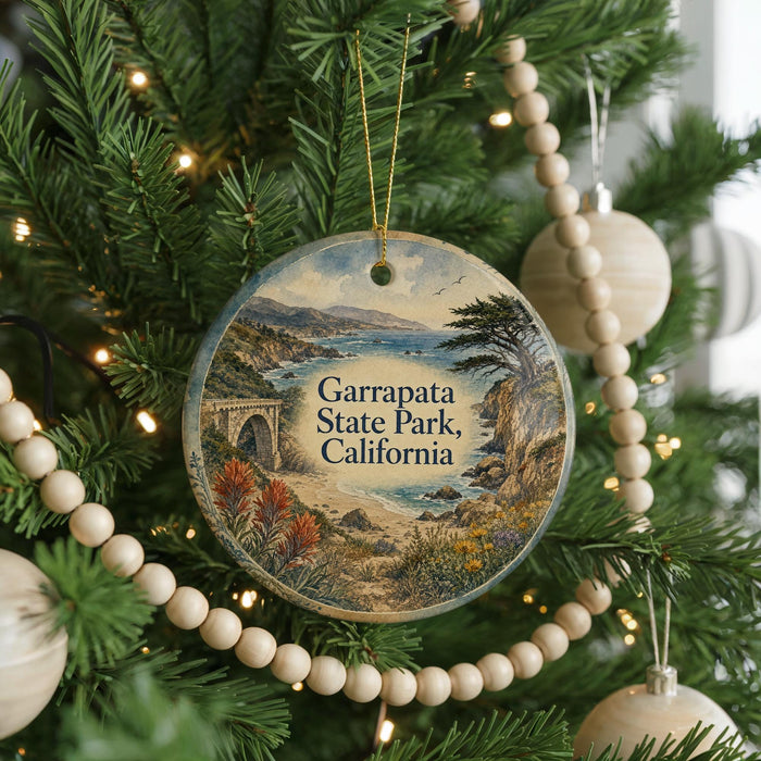 A round ornament hanging on a Christmas tree, featuring a scenic landscape with a bridge and mountains in the background.