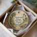 A round ornament with a lighthouse and palm trees, placed in a box with a white tissue paper lining.