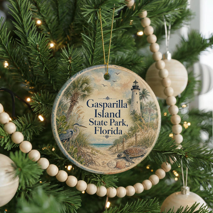 A round ornament hanging on a Christmas tree, featuring a lighthouse and palm trees, with the text "Gasparilla Island State Park, Florida" displayed on it.