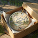 A decorative ornament in a wooden box, featuring a lighthouse and palm trees, with the text "Gasparilla Island State Park, Florida" printed on it.