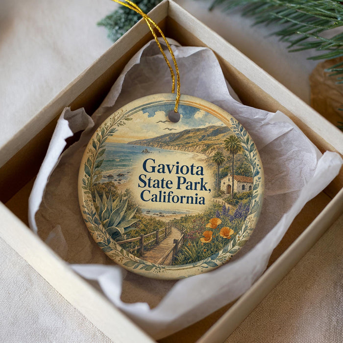 A decorative ornament in a box, featuring a scenic landscape with a beach, mountains, and a small building.