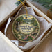 A decorative ornament in a box, featuring a scenic landscape with a waterfall, flowers, and a bridge.