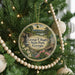 A round ornament hanging on a Christmas tree, featuring a scenic landscape with a waterfall and flowers.