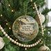 A round ornament hanging on a Christmas tree, featuring a scenic landscape with a bridge and a deer.