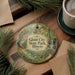 A decorative ornament with the text "Giant City State Park, Illinois" on it, surrounded by pine branches and a cup of coffee on a wooden surface.