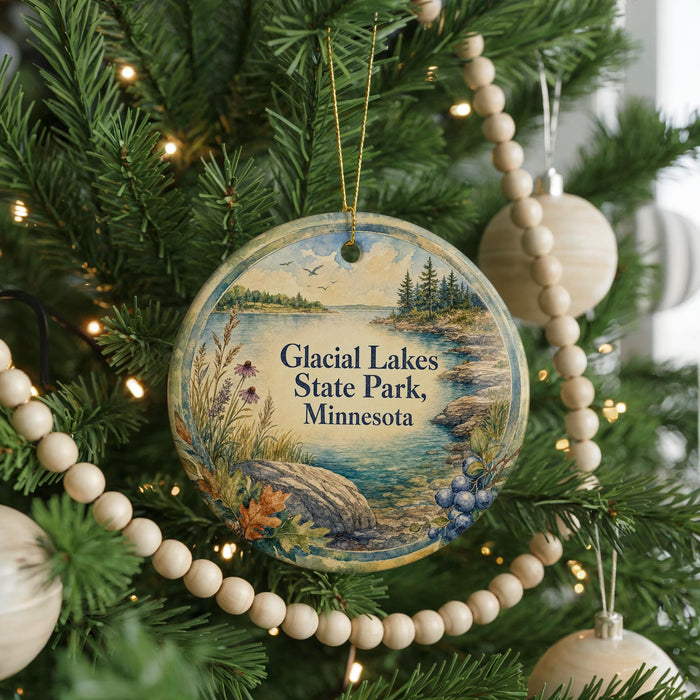 A circular ornament hanging on a Christmas tree, featuring a scenic landscape with a lake and mountains.