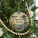 A circular ornament hanging on a Christmas tree, featuring a scenic landscape with a lake and mountains.