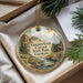 A decorative ornament with a scenic landscape of mountains, trees, and a cabin, hanging from a string.