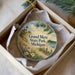A decorative ornament in a box, featuring a scenic landscape with a lighthouse and a beach, with the text "Grand Mere State Park, Michigan" printed on it.