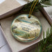 A decorative ornament in a box, featuring a scenic image of the beach and park in Florida.