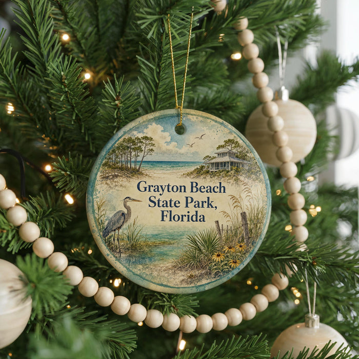 A round ornament hanging on a Christmas tree, featuring a scenic image of a beach and a bird.