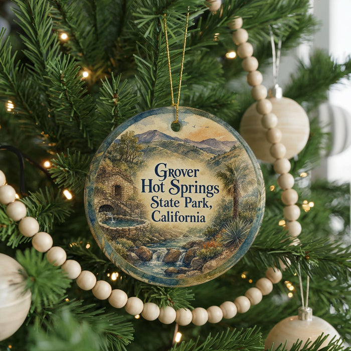 A round ornament hanging on a Christmas tree, featuring a scenic landscape with mountains, a waterfall, and palm trees.