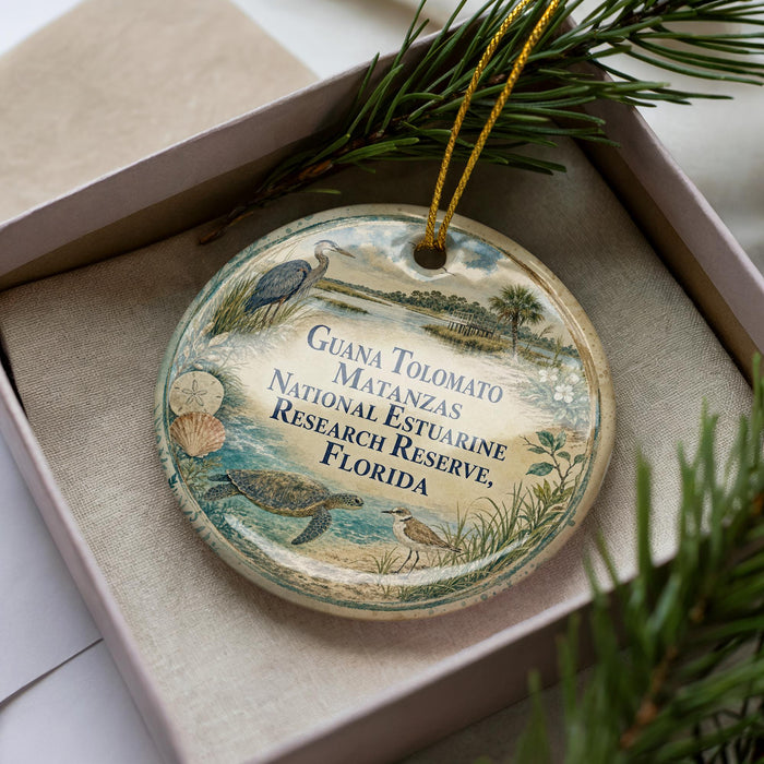 A decorative ornament in a box, featuring a bird, a turtle, and other natural elements, with text that reads "Guana Tolomato Matanzas National Estuarine Research Reserve, Florida".