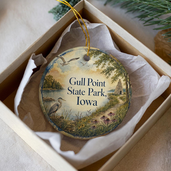 A decorative ornament in a white box, featuring a serene landscape with a bird, trees, and a body of water.