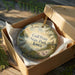 A decorative ornament in a wooden box, featuring a scenic landscape with birds and greenery, with the text "Gull Point State Park, Iowa" printed on it.