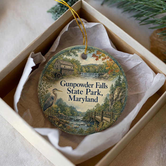 A round ornament with a scenic image of Gunpolder Falls State Park, Maryland, displayed in a box with a white tissue paper lining.